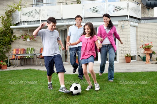 Cute kids playing football with their parents at backyard